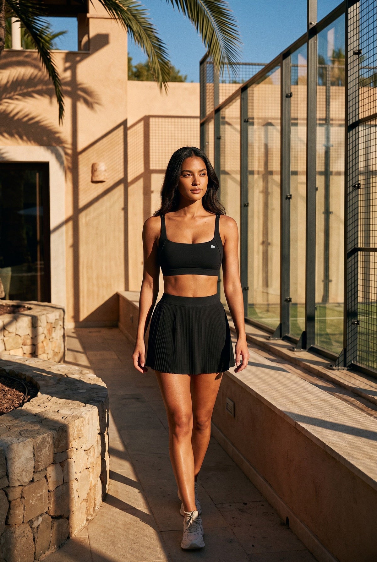 CORA bra top & pleated skirt set in Black – women's padel set by Six'o – lifestyle photo at the padel club