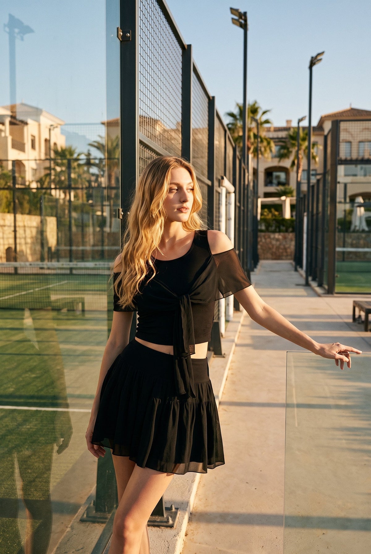 LILA cold-shoulder top & tiered skirt set in Black – women's padel set by Six'o – lifestyle photo at the padel club