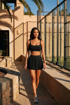 CORA bra top & pleated skirt set in Black – women's padel set by Six'o – lifestyle photo at the padel club