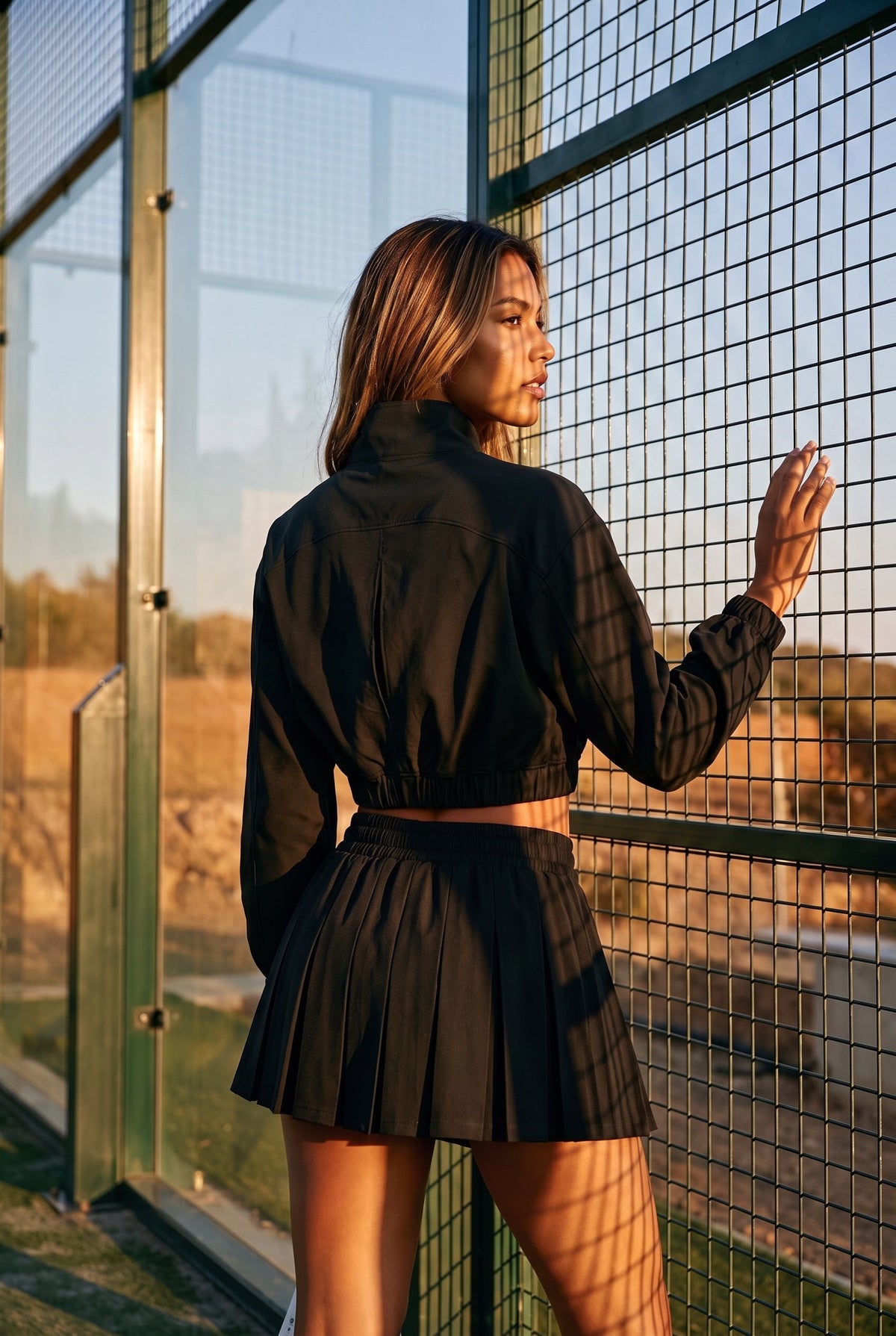 ELSA cropped jacket & pleated skirt set in Black – women's padel set by Six'o – lifestyle photo at the padel club